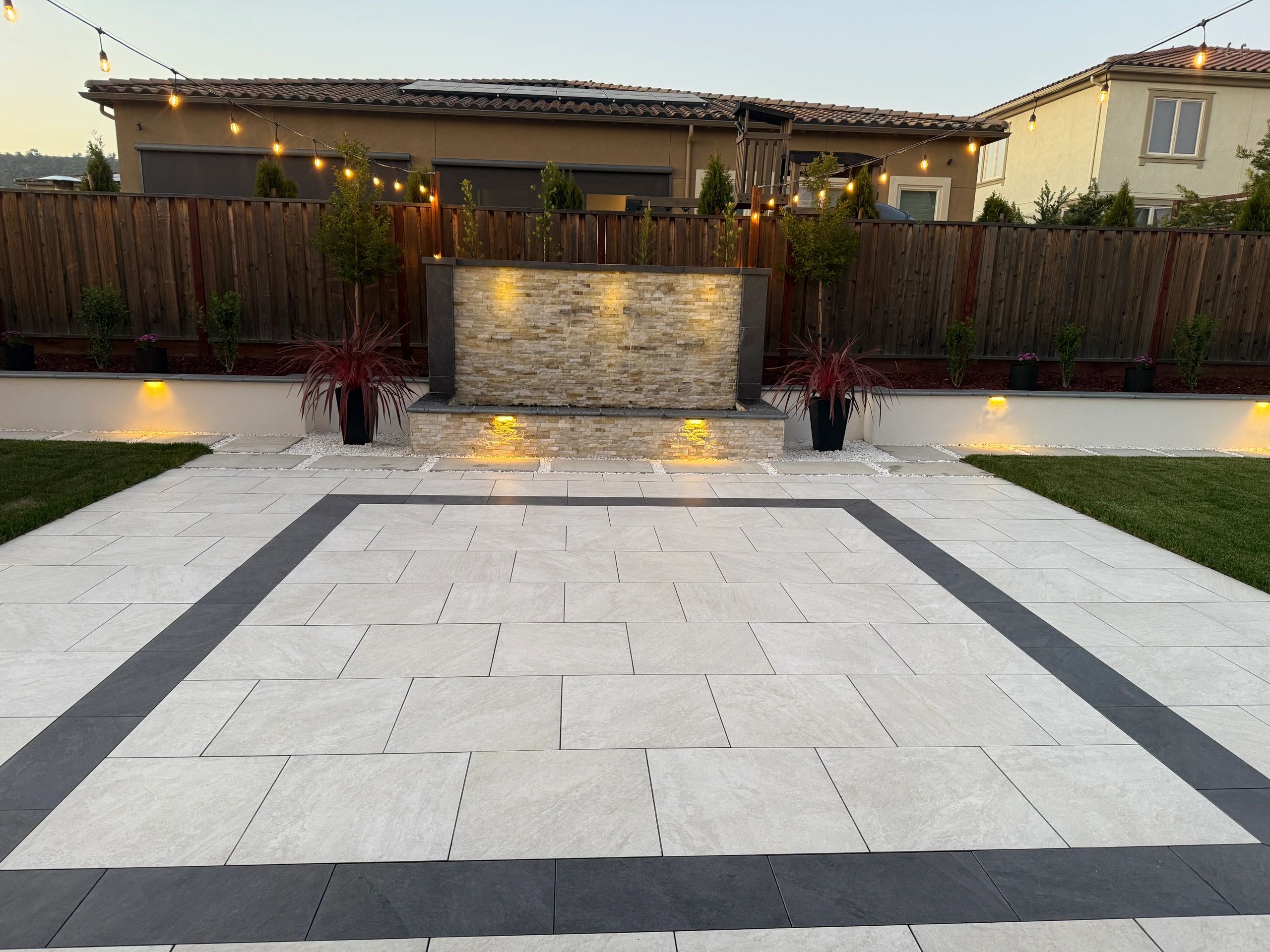 Modern backyard with stone patio and lights.