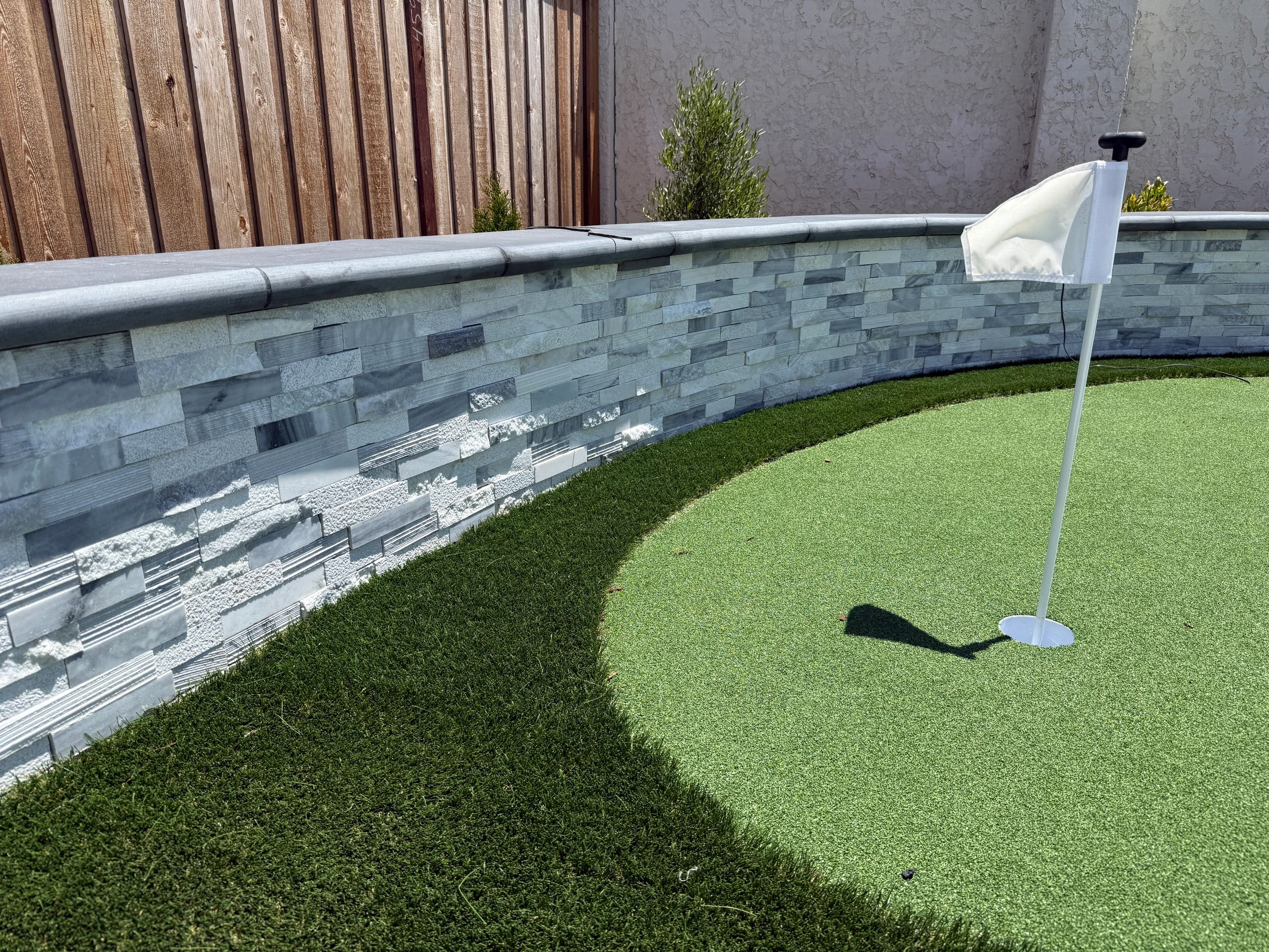 Putting green with flag and stone wall.
