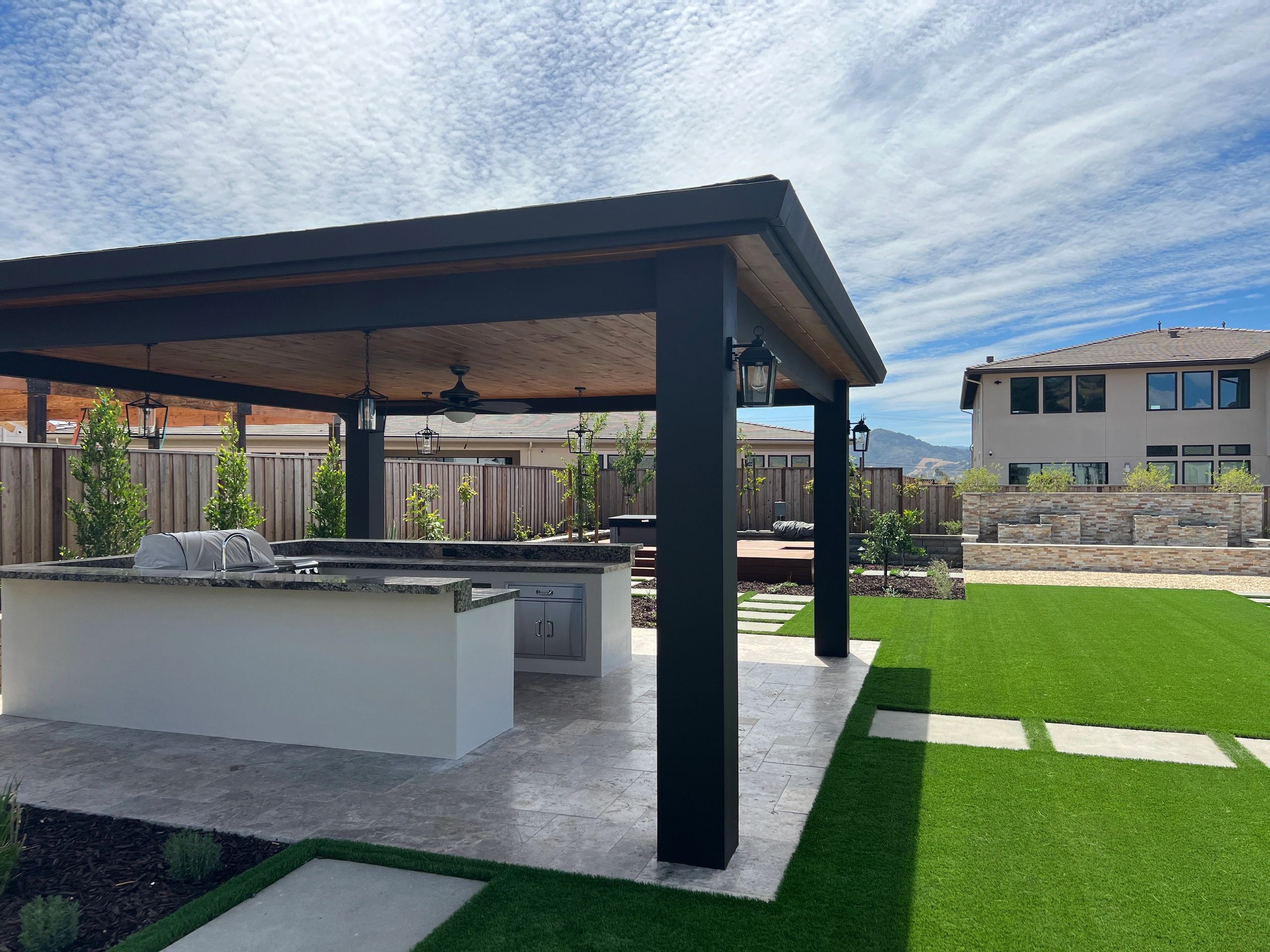 Outdoor kitchen with pergola and green lawn.